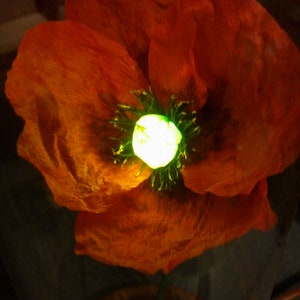 K&ouml;nnte beinhalten: Nahaufnahme einer roten Mohnblume mit einem leuchtend gr&uuml;nen Zentrum. Die Blume ist aus Papier und hat eine strukturierte Oberfl&auml;che.