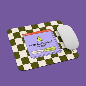 Op de afbeelding: Een rechthoekige muismat met een groen en wit geblokt patroon. De mat heeft een pop-up venster grafiek met de tekst "PERFECTIONIST ALERT" en een muiscursor over de "DECLINE" knop. Een witte muis staat rechts.