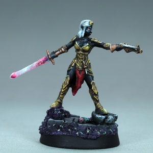 Può includere: Una statuetta in miniatura dipinta di una guerriera elfa femminile che indossa un'armatura dorata e una gonna rossa, tenendo una spada e una pistola. La statuetta è in piedi su una base nera con una texture di pietra viola e verde.