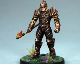 May include: A miniature figure of a warrior wearing gold and brown armor, holding a flaming torch. The figure is standing on a black base with green and purple foliage.