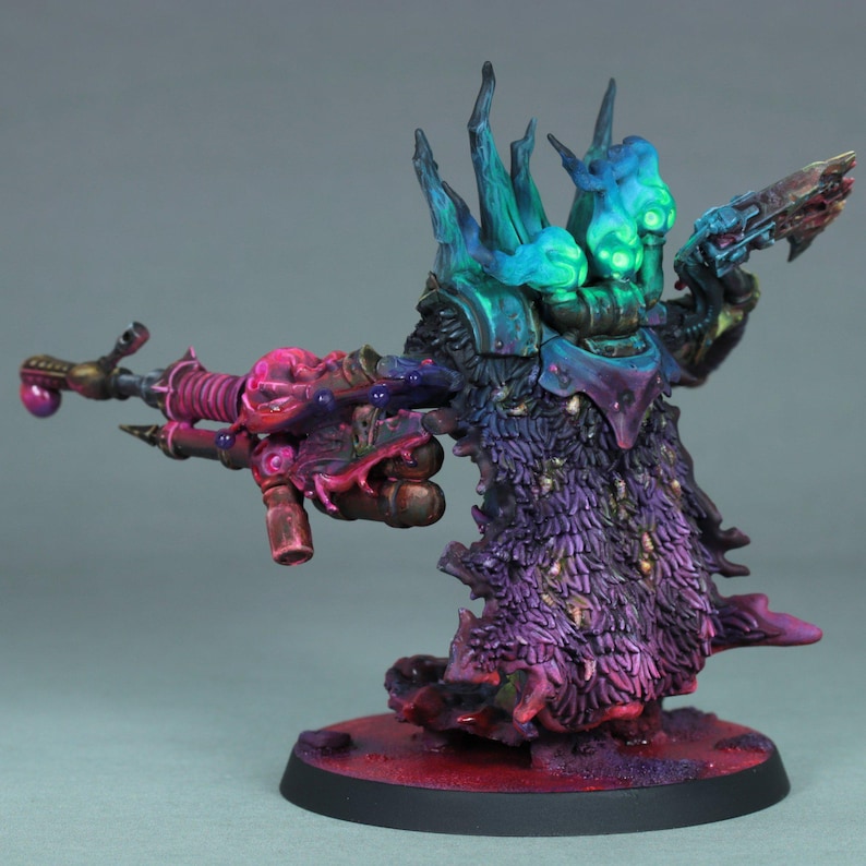 May include: A miniature figure of a fantasy character, painted with vibrant colors. The figure has a multi-colored head with teal and blue accents, a purple and pink cloak, and is holding a weapon. The base is red.
