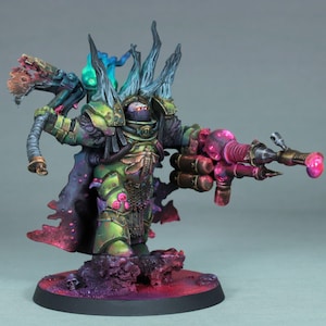 May include: A detailed miniature figure of a warrior in green and bronze armor, holding a large weapon with pink and red accents. The figure has a dark cloak and is standing on a textured base with purple and red tones.