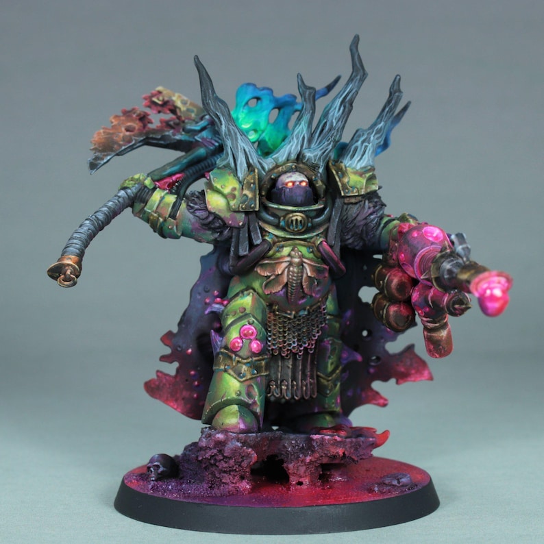 May include: A detailed miniature figure of a warrior in green and gold armor, holding a weapon. The figure has a dark cloak and is set on a base with purple and red accents. The figure's head is obscured by a helmet.