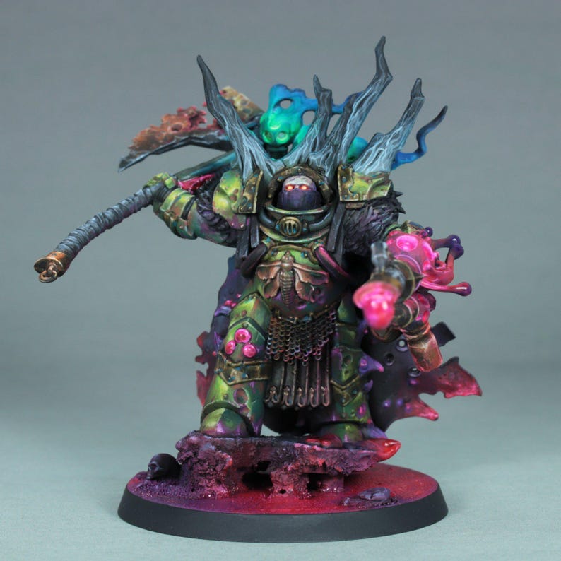 May include: A detailed miniature figure of a warrior in green and gold armor, holding a staff and a weapon that emits pink energy. The figure stands on a base with a dark red and purple color scheme, with a gray background.