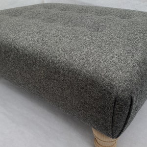 May include: A grey fabric footstool with wooden legs. The footstool has a tufted top and a simple design.