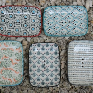 Könnte beinhalten: Fünf Keramik-Seifenschalen mit verschiedenen Mustern. Die Schalen sind rechteckig und haben einen weißen Hintergrund mit verschiedenen farbigen Designs. Die Designs umfassen florale, geometrische und abstrakte Muster.