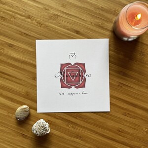 May include: A white card with a red and white mandala design. The mandala is a symbol of the root chakra, Muladhara. The text on the card reads "root - support - base".