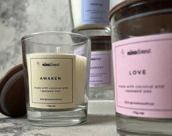 Könnte beinhalten: Mehrere Glas-Kerzengläser mit Holzdeckeln. Die vordere Kerze trägt die Aufschrift "AWAKEN" und "made with coconut and rapeseed wax". Die Kerzen sind mit cremefarbenem Wachs gefüllt und haben ein Nettogewicht von 72g.