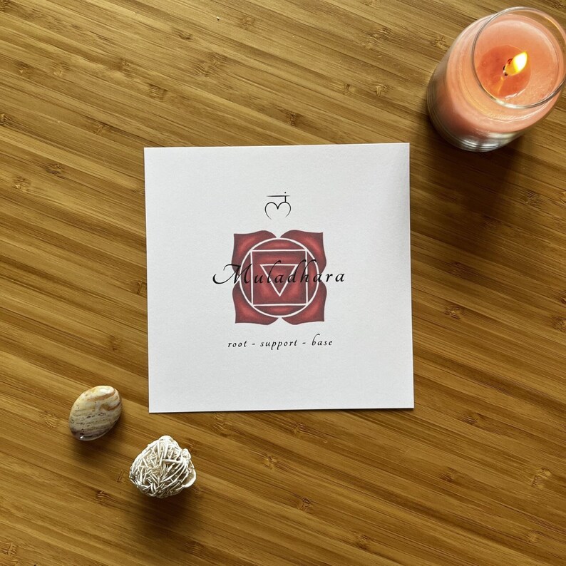 May include: A white card with a red and white mandala design. The mandala is a symbol of the root chakra, Muladhara. The text on the card reads "root - support - base".
