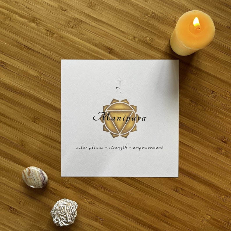 May include: A white card with a yellow and gold symbol, the text "Manipura", and the words "solar plexus - strength - empowerment".