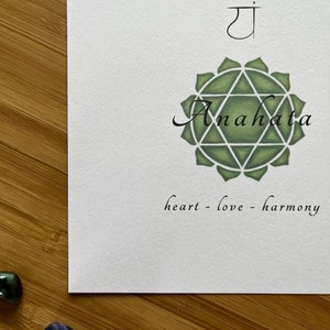 May include: A green and white illustration of the Anahata chakra, the heart chakra, with the Sanskrit symbol "ya" above it. The text "heart - love - harmony" is below the illustration.
