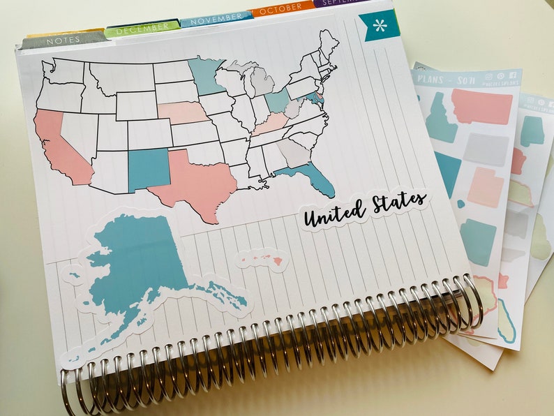 May include: A spiral-bound planner with a United States map sticker, featuring states in various colors. The sticker reads "United States." Additional state stickers are visible. Tabs for months like December and November are at the top.