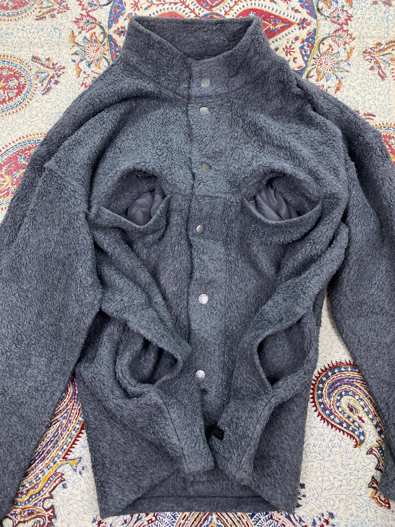 May include: A gray fleece jacket with a high collar and snap closures. The jacket has two large front pockets and a soft, textured appearance. The sleeves are long and the overall design is casual and warm.
