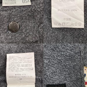 May include: Close-up of a gray Gramicci jacket with multiple tags. The tags include the brand name, size "M", and care instructions. The jacket is made of a soft, textured material.