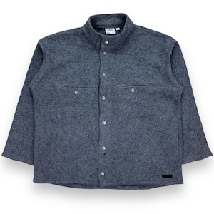 May include: A dark gray fleece jacket with a button-up front, two chest pockets, and a stand-up collar. The jacket has a textured appearance and a small black label near the bottom.