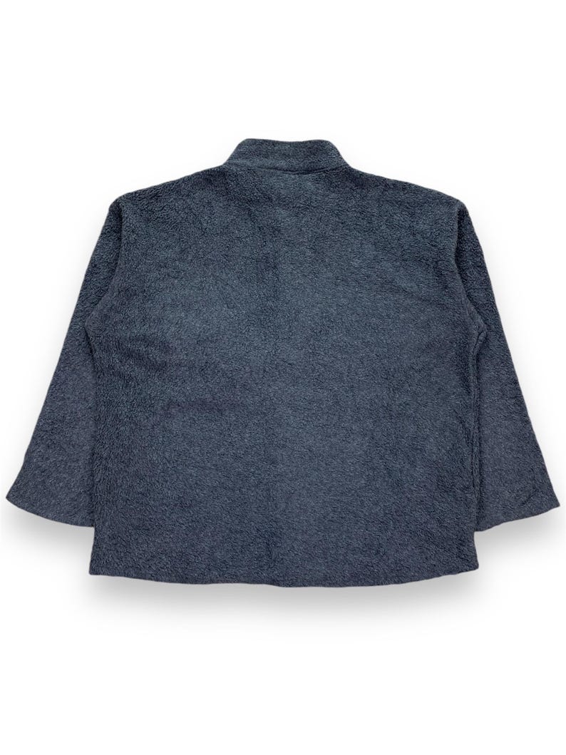 May include: A dark gray fleece jacket with a high collar and long sleeves. The jacket has a soft, textured appearance and a relaxed fit. The back view of the jacket is shown against a white background.