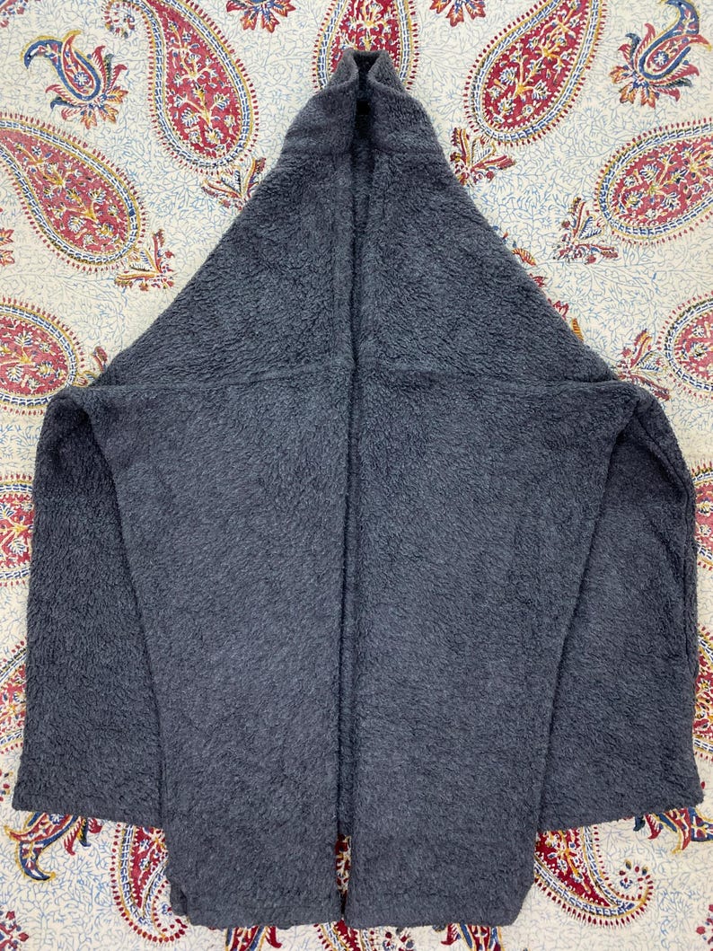 May include: A dark gray, hooded fleece jacket. The jacket is made of a soft, textured material and features a large hood and open front. The jacket is laid flat on a patterned surface.