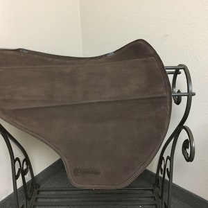 May include: A brown suede saddle pad with a black leather trim and the word "Contoured" printed on the bottom.