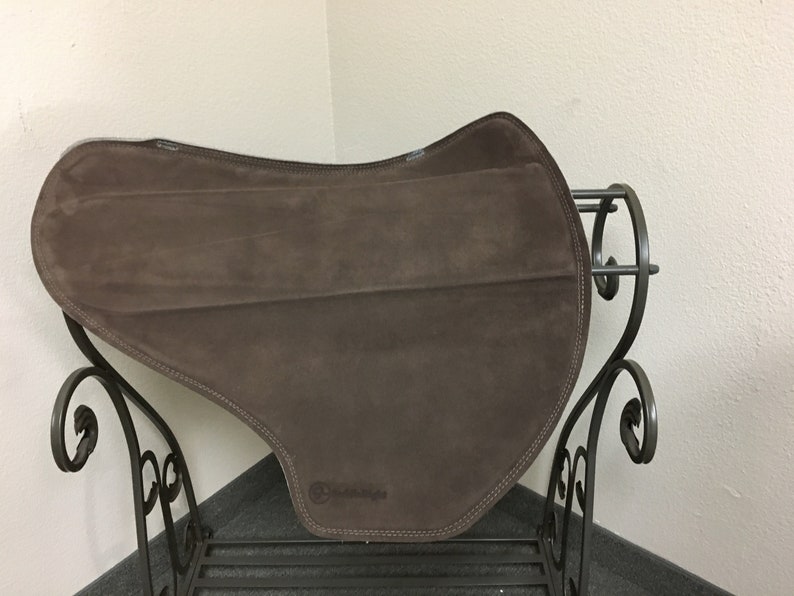 May include: A brown suede saddle pad with a black leather trim and the word "Contoured" printed on the bottom.