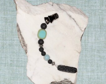 May include: A black lava stone and turquoise bead necklace with a silver clip and a silver bead. The necklace is on a white marble surface.