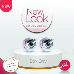 May include: Pair of dark gray glass eyes for doll making. The eyes are on a white platform with a pink base. The eyes have a silver rim and black eyelashes. The text "New Look Stationary Glass Eyes" is on a pink circle above the eyes. The text "Dark Gray" is below the eyes. The text "THE ORIGINAL TEMPERED GLASS EYES PREMIUM" is on a pink circle with white stars. The text "DK" is on a pink circle.