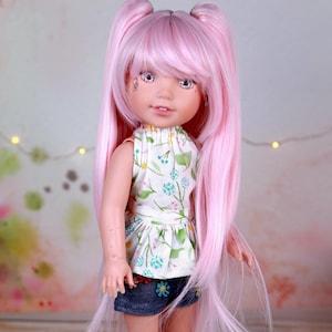 May include: A doll with long pink hair styled in pigtails, wearing a white floral top, denim shorts with flower embroidery, and white sneakers. The doll has a fair complexion and is posed against a soft, blurred background.