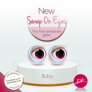 Op de afbeelding: Een paar robijnrode glazen ogen voor poppen, met een zilveren rand en zwarte pupillen. De ogen staan op een wit voetstuk met de tekst "New Swap On Eyes The First tempered glass" en "Ruby" eronder. De tekst "DK" staat in een roze cirkel.