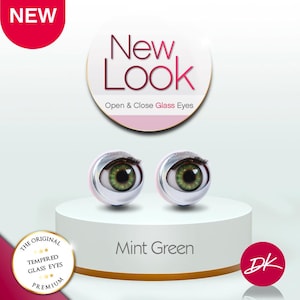 May include: Two mint green glass eyes with black eyelashes, displayed on a white pedestal. The image includes text that reads "New Look Open & Close Glass Eyes" and "Mint Green". A red circle with the word "NEW" is in the upper left corner.