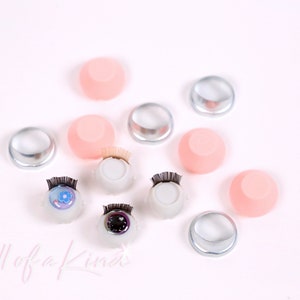 May include: Assortment of doll eye supplies including clear plastic eye sockets, pink silicone eye sockets, and two sets of doll eyes with lashes.