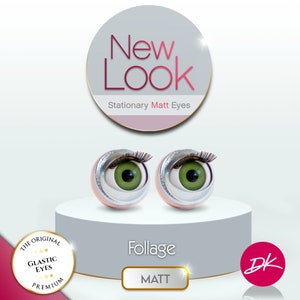 Peut inclure: Une paire d'yeux en verre vert avec des cils noirs et des cercles argentés. Les yeux sont sur une plateforme blanche avec une base rose. Le texte "New Look" est dans un cercle au-dessus des yeux. Le texte "Stationary Matt Eyes" est sous les yeux. Le texte "Foliage" est sous la plateforme. Le texte "MATT" est dans un rectangle argenté sous le texte "Foliage". Le texte "DK" est dans un cercle rose à droite de la plateforme.