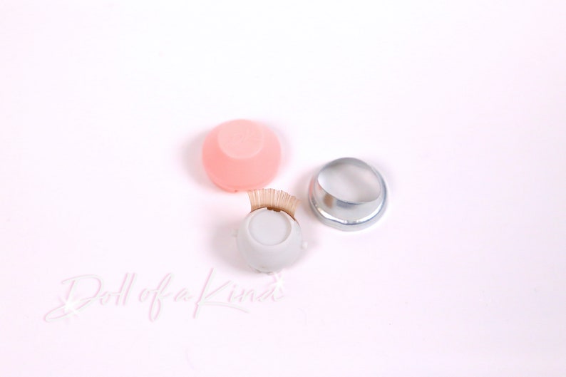 May include: Three doll eye making tools: a pink silicone eye socket, a white plastic eye socket with a row of lashes, and a silver metal eye socket.