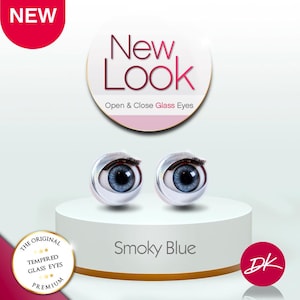 May include: Two Smoky Blue open and close glass eyes with black eyelashes are displayed on a white pedestal. The text "New Look" and "Open & Close Glass Eyes" are above the eyes. The text "Smoky Blue" is below the eyes.