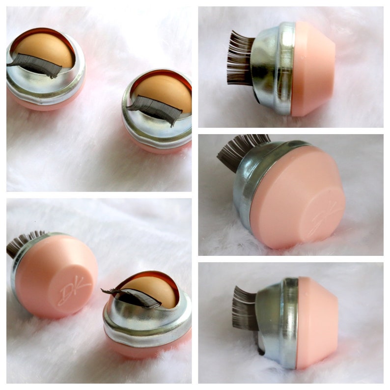 May include: Five pink and silver containers with a brush of black lashes sticking out of the top. The containers have a silver band around the middle and a pink lid. The containers are on a white surface.