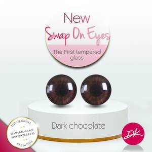 May include: Two dark chocolate-coloured, glass doll eyes are displayed on a white pedestal. The text "New Swap On Eyes" and "The First tempered glass" are above the eyes. The text "Dark chocolate" is below the eyes. A circular logo reads "The Original Tempered Glass Swappable Eyes Premium".