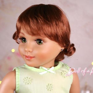 May include: A doll with auburn hair styled in pigtails and green eyes. The doll wears a light green dress with flower and bow details. The doll's face is detailed with makeup, and the background is softly blurred with bokeh lights.