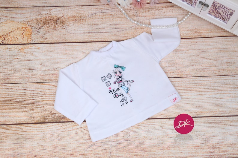 May include: White long-sleeve shirt with a graphic of a girl holding a shopping cart and the text "Nice Day".