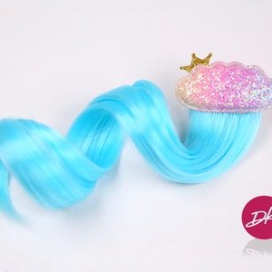 Puede incluir: Una extensión de cabello azul claro con una nube rosa brillante con una corona dorada en la parte superior. La extensión de cabello está rizada y está unida a la nube.