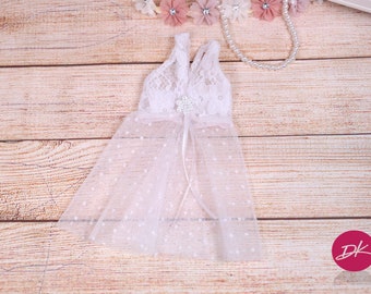 Può includere: Abito bianco in pizzo e tulle con pois bianchi. L'abito ha una scollatura a V e un fiocco di fiori bianco al centro.