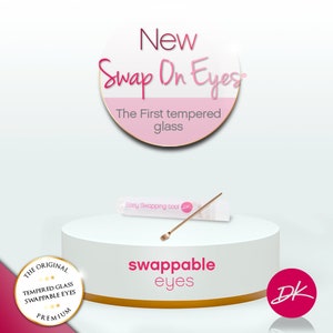 May include: New Swap On Eyes, the first tempered glass swappable eyes. A pink and gold circle with the text "New Swap On Eyes" and "The First tempered glass". A white surface with a pink and gold circle with the text "THE ORIGINAL TEMPERED GLASS SWAPPABLE EYES PREMIUM". A white surface with a pink and gold circle with the text "swappable eyes". A white surface with a pink and gold circle with the text "DK". A white surface with a clear tube labeled "Easy Swapping tool" with a gold tool inside.