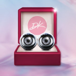 May include: A red velvet ring box with the initials "DK" on the lid. Inside the box are two silver cufflinks with a realistic eye design.