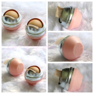May include: Five pink and silver eyelash extension applicators with a brush on the top. The applicators are round and have a silver lid. The applicators are on a white fluffy surface.