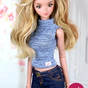 May include: A doll with long, wavy blonde hair wearing a blue and gray sleeveless turtleneck top and dark blue jeans.