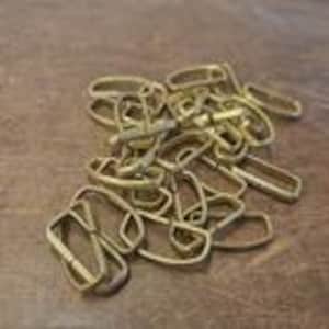 May include: A collection of gold-coloured metal chain links on a brown wooden surface. The links are various shapes and sizes, including rectangular and oval. The chain appears to be new and unused.