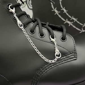 May include: Black leather boots with a silver chain and two silver charms attached to the laces. The charms are in the shape of a hand.