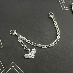 May include: A silver chain with two clasps and a silver moth charm. The chain is double-stranded and has a delicate, intricate design.