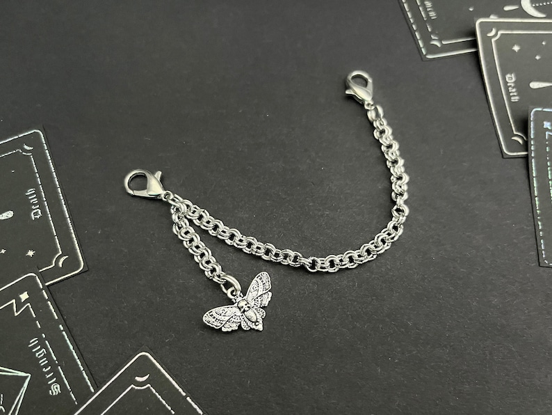 May include: A silver chain with two clasps and a silver moth charm. The chain is double-stranded and has a delicate, intricate design.