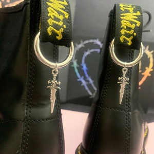 May include: A pair of black leather boots with silver sword charms attached to the laces. The boots have yellow and black striped straps with the text "Air Max" printed on them.