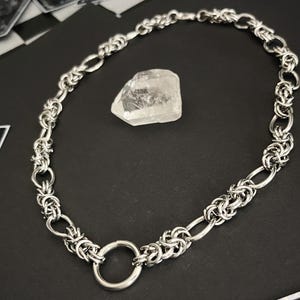 K&ouml;nnte beinhalten: Eine silberne Kettenkette mit einem gro&szlig;en, runden, offenen Ringverschluss. Die Kette besteht aus ineinandergreifenden Metallringen.