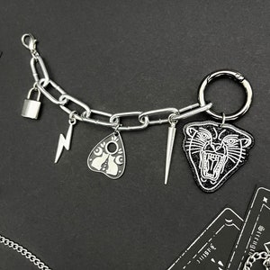 May include: A silver chain bracelet with charms, including a padlock, lightning bolt, a Ouija board, a dagger, and a black and white panther head.
