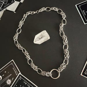 K&ouml;nnte beinhalten: Eine silberne Kettenkette mit einem gro&szlig;en, runden, silbernen Ringverschluss. Die Kette besteht aus ineinandergreifenden Metallgliedern.